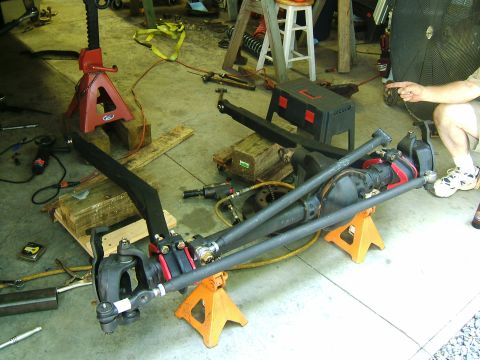 1993 Ford Bronco - A disassembled front axle assembly, likely for an off-road vehicle, sits on jack stands in a garage with tools around.