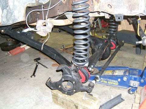 1993 Ford Bronco - Close-up view of vehicle suspension components, including a large coil spring and steering linkage, undergoing repair.