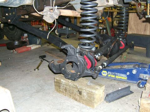 1993 Ford Bronco - Close-up of vehicle suspension parts and springs, supported by wooden blocks and a hydraulic jack.