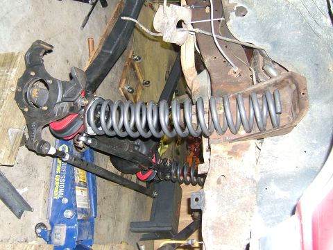 1993 Ford Bronco - Close-up of a vehicle's front suspension system, coil springs and red bushings, supported by a blue hydraulic jack.