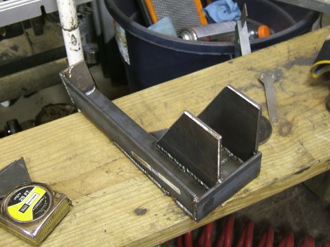 1993 Ford Bronco - A custom metal bracket is shown on a workbench, with tools and a tape measure nearby.