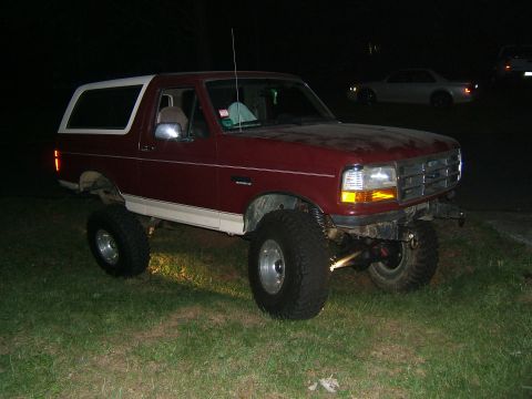 1993 Ford Bronco - A lifted, maroon and white Ford Bronco sits on a grassy area under the night sky.