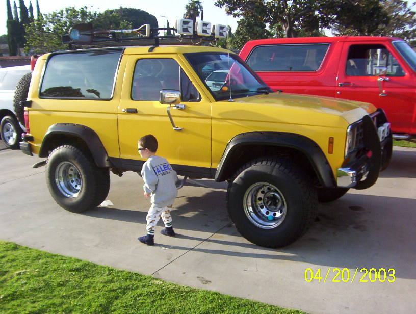 Yellow lifted two-door Ford Bronco II with roof lights, child walking beside it