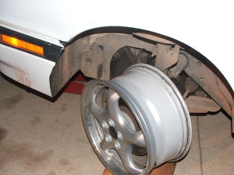 1990 Dodge Shadow - A car's wheel is off, revealing the inner workings of the fender and suspension system.