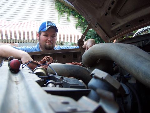 1987 Ford Bronco - A mechanic works on the engine of a vehicle, with the hood open and various engine parts visible.