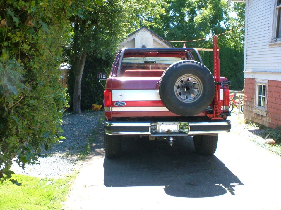 1989 Ford Bronco rear view, red with white stripe, spare tire on back, red Hi-Lift jack attached