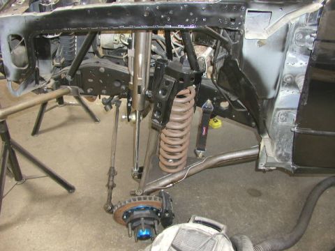 1984 Ford Bronco - Close-up view of the front suspension and chassis of a vehicle, showing a large coil spring, shock absorber, and steering linkage.
