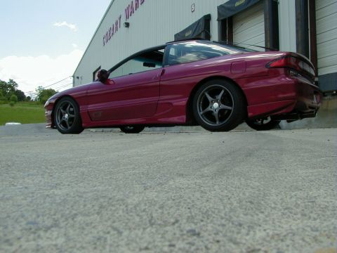 1994 Ford Probe - A maroon coupe with aftermarket wheels is parked outside a warehouse. The vehicle has a GT badge on its side.
