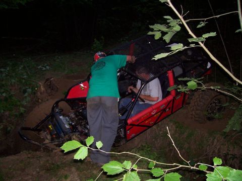 1989 Ford Bronco II - A red off-road buggy is stuck in a muddy ditch with two occupants visible.