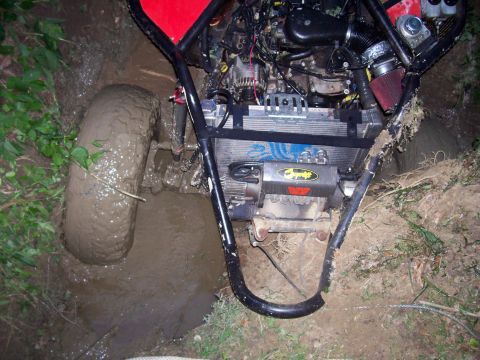 1989 Ford Bronco II - An off-road vehicle is stuck in a muddy ditch, with its engine and radiator exposed.