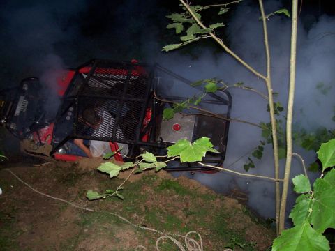 1989 Ford Bronco II - An off-road buggy has tipped onto its side in a wooded area, emitting smoke.