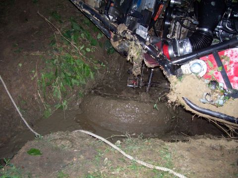 1989 Ford Bronco II - An off-road vehicle is deeply stuck in a muddy pit, with only its frame and engine components visible above the mire.