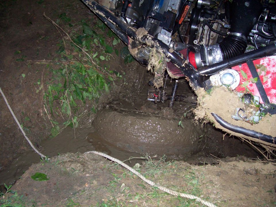 Off-road vehicle with red bodywork stuck deep in mud, front tire submerged