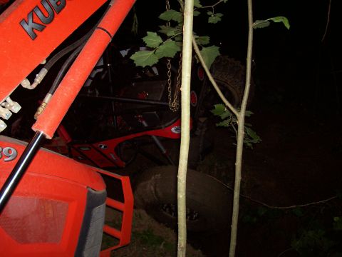 1989 Ford Bronco II - An overturned red off-road vehicle lies in the mud, with a tractor visible in the foreground.