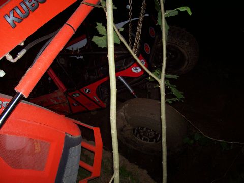 1989 Ford Bronco II - An orange tractor is parked next to a black off-road vehicle, partially obscured by trees at night.