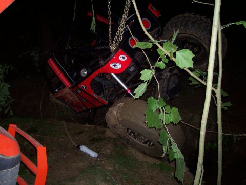 1989 Ford Bronco II - Off-road vehicle is stuck in the mud, tilted at an angle with chains attached.