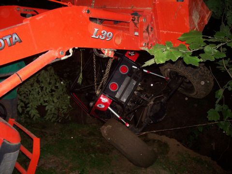 1989 Ford Bronco II - An off-road vehicle is suspended by a tractor's loader arm after getting stuck in the mud.
