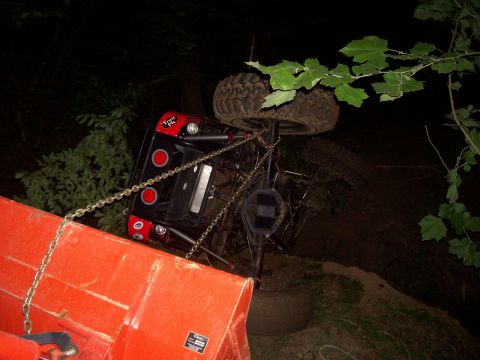 1989 Ford Bronco II - An overturned red off-road vehicle is being pulled by an orange piece of equipment at night.