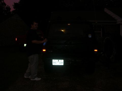 1989 Ford Bronco II - Man with spray can near the back of a dark SUV at night. License plate is visible.