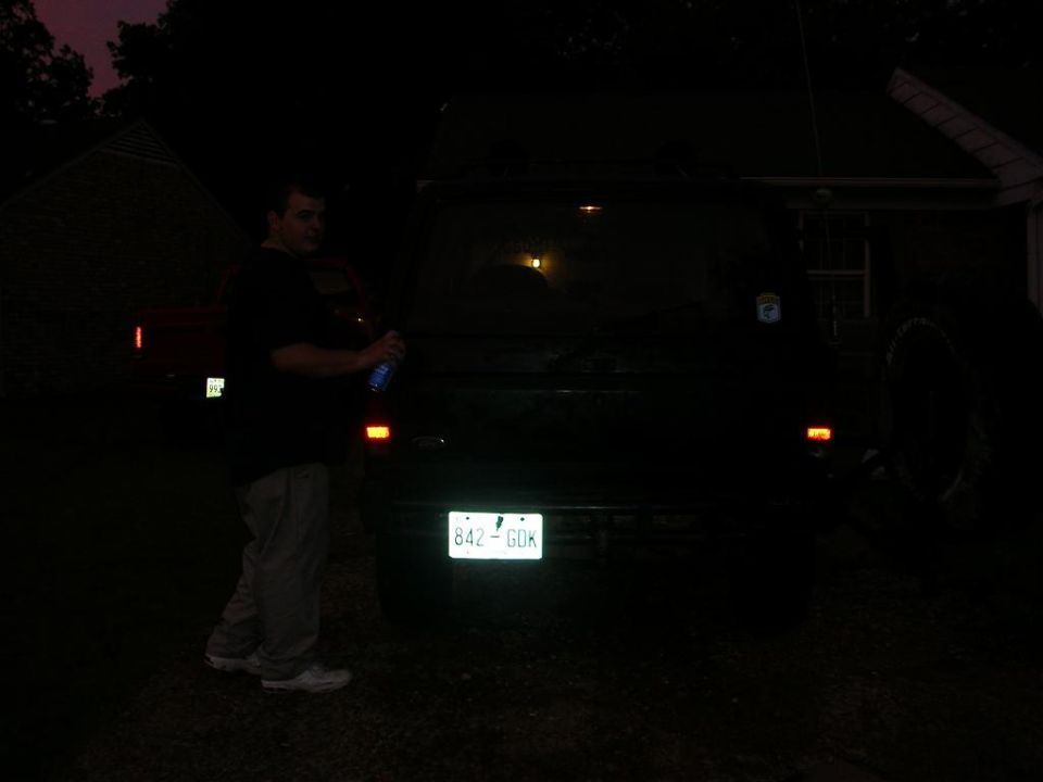 Man holding a spray can next to the rear of a dark SUV with license plate 842-GDK
