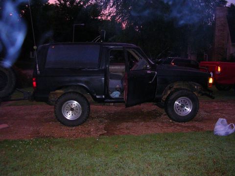 1989 Ford Bronco II - A black SUV sits with its doors open as smoke billows from its side, with another vehicle visible in the background.