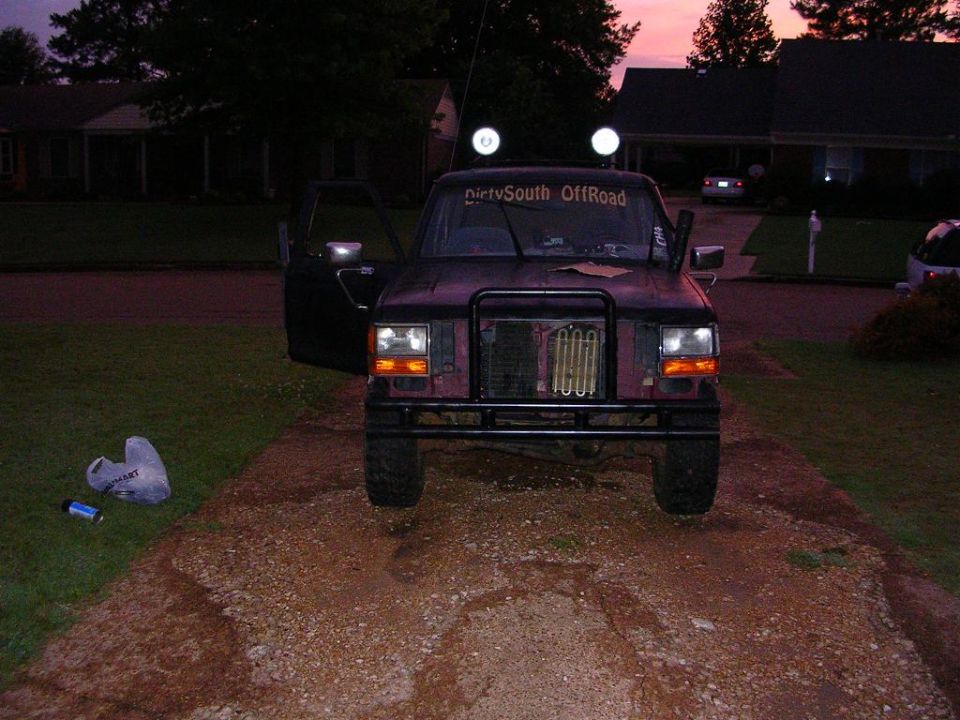 Dark purple 1989 Ford Bronco II with aftermarket grille guard and off-road lights, parked on a gravel driveway