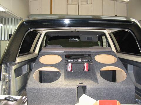 1991 Ford Bronco - The rear interior of a vehicle shows a large, custom-built enclosure housing a stereo and speaker cutouts.