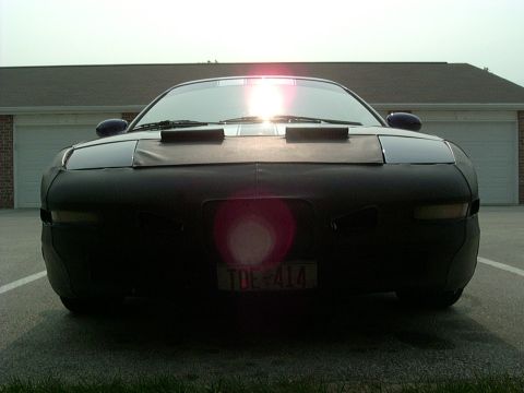 1995 Ford Probe - A car is parked in front of a garage, its front end covered by a black fabric car cover.