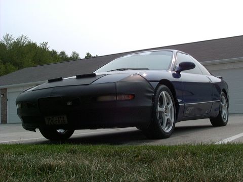 1995 Ford Probe - A blue coupe is parked outside a house, partially covered by a car bra on its front end.