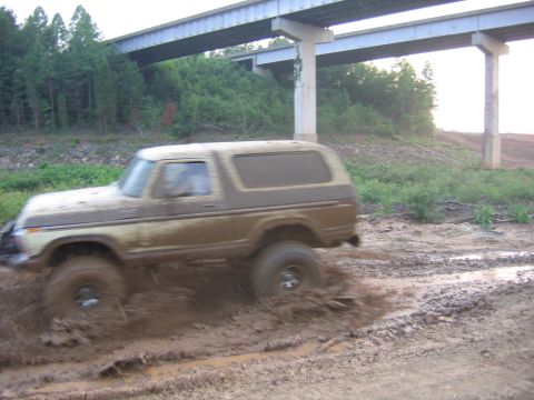 1992 Ford Mustang - A muddy Ford Bronco navigates a treacherous off-road path beneath a concrete overpass.