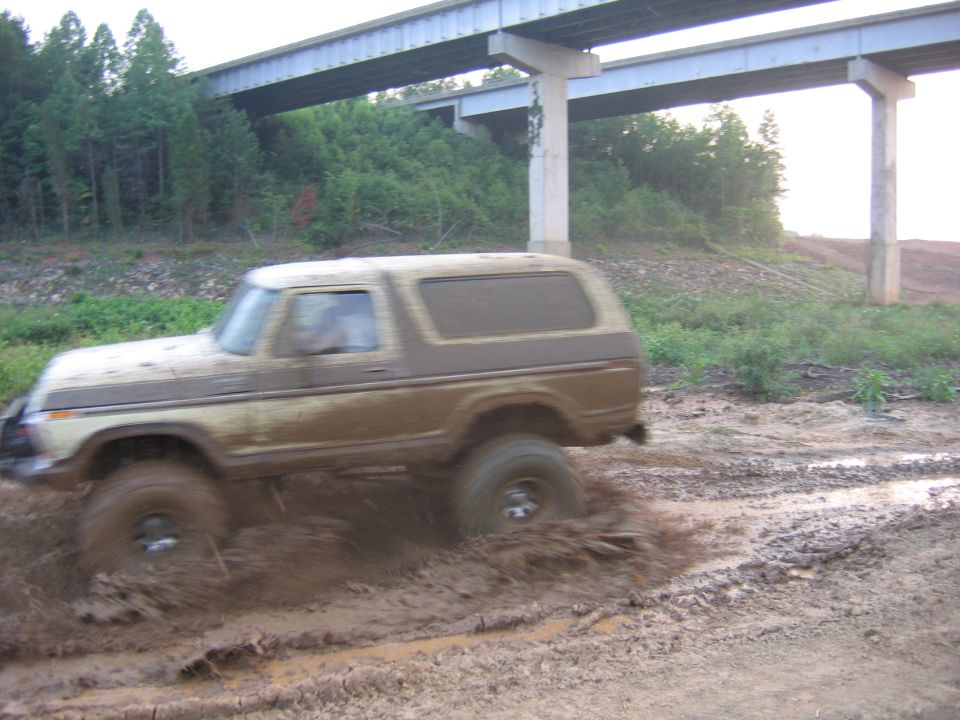 Brown Ford Bronco driving through mud under a highway overpass