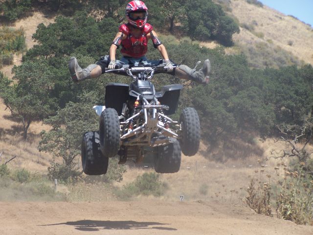 Person in full gear jumps an ATV mid-air with legs spread wide