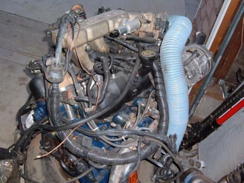 1985 Ford Bronco II - Engine assembly with blue hoses and wiring harnesses, showing an alternator and intake manifold.
