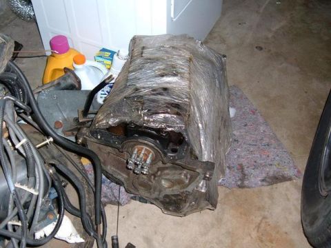 1985 Ford Bronco II - Engine block wrapped in plastic, stored with other automotive parts and cleaning supplies.