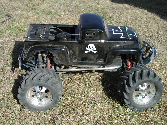 Black RC monster truck with pickup body, skull decal, Iron Cross graphic, big tires on chrome wheels, parked on grass