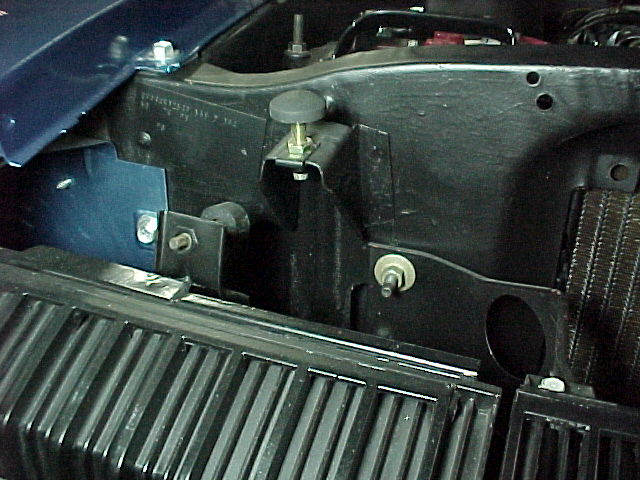 Engine bay detail showing black radiator support, brackets and bolts with radiator fins below