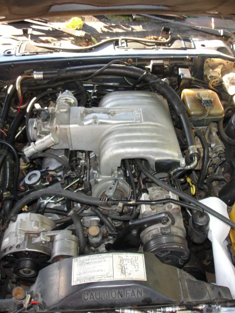 1989 Lincoln Continental - Close-up view of a vehicle's engine bay, a prominent intake manifold and fan warning label.