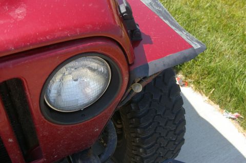 1998 Jeep TJ - Close-up of a red Jeep TJ's front fender, showing the headlight and tire tread.