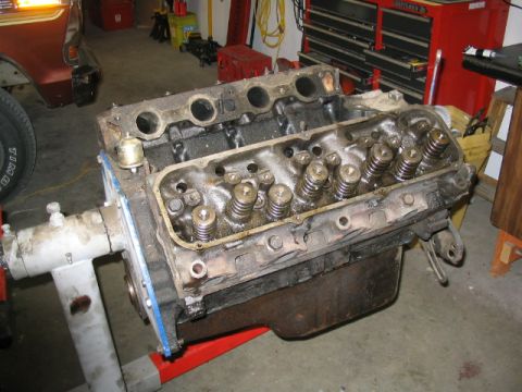1979 Ford F-150 - A V8 engine block is mounted on an engine stand in a garage setting, with tools and a vehicle in the background.