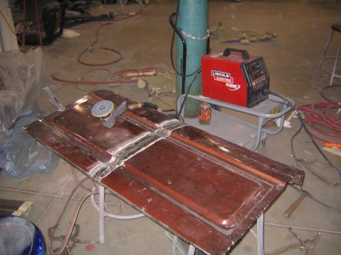 1982 Ford Bronco - A car door is being worked on with a grinder and welding equipment in a garage setting.