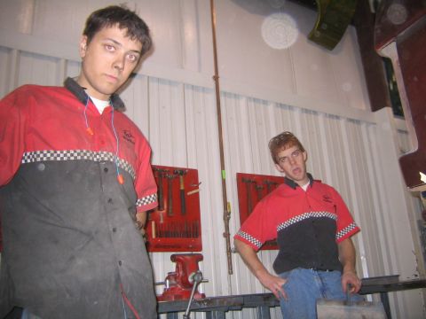 1982 Ford Bronco - Two men in work uniforms pose in a workshop setting with tools displayed on the wall behind them.
