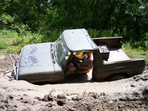 1979 Ford Bronco - A man drives an olive green pickup truck that is stuck deep in mud.