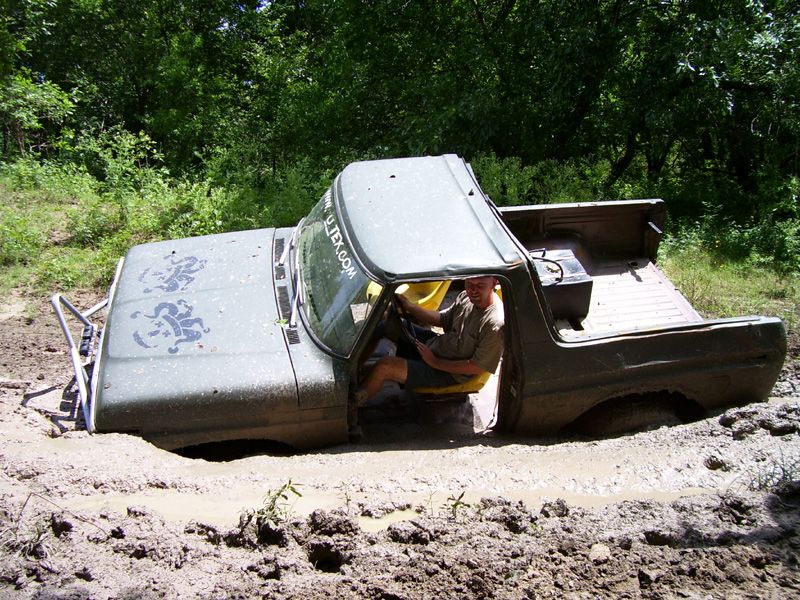 Olive green pickup truck stuck in mud with a man driving