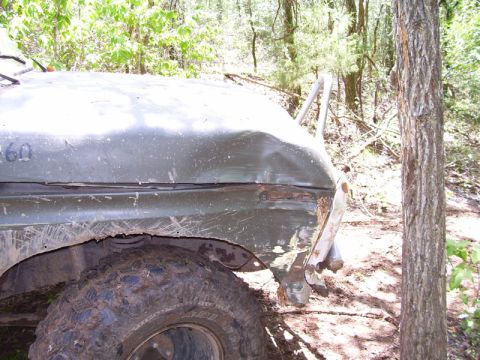 1979 Ford Bronco - Vehicle fender and tire visible in a wooded area, showing damage and mud.