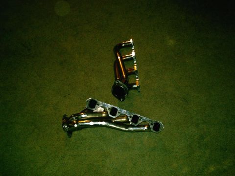 2001 Dodge 2500 - Two exhaust manifolds are displayed on a green surface. The website Supermotors.net is visible in the lower right corner.