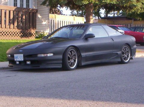 1993 Ford Probe - A matte black 1993 Ford Probe is parked on a residential street with a red car visible behind it.