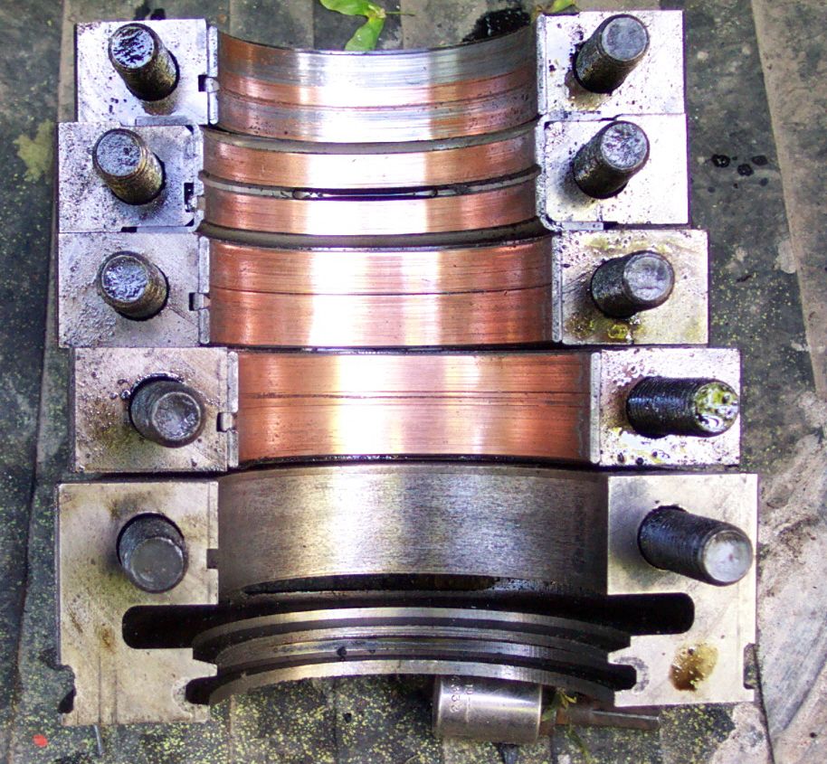 Engine bearing caps with copper inserts and a crankshaft pulley. The caps are bolted to metal blocks