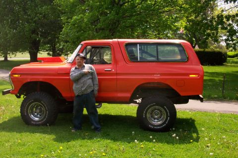 1978 Ford Bronco - A man poses with his lifted red 1978 Ford Bronco, modified with larger tires and wheels.