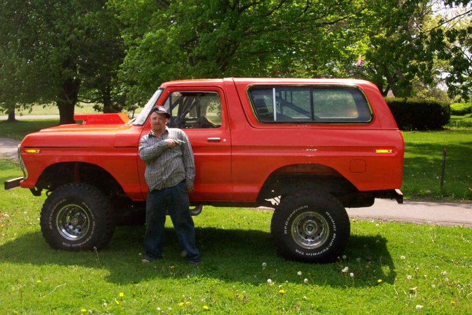 Man standing next to a red 1978 Ford Bronco with aftermarket wheels and tires