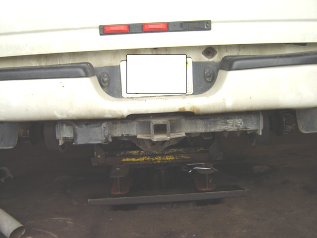 Back of a white truck with a trailer hitch and a license plate area covered by a white box